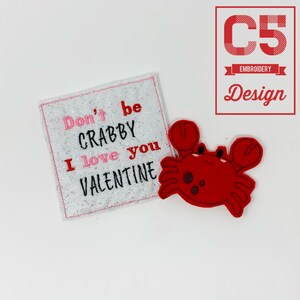 May include: A white square patch with glitter and the text "Don't be Crabby I love you Valentine" in pink and black embroidery. A red felt crab is next to the patch.