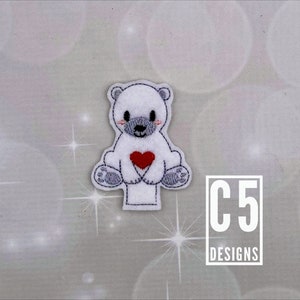 May include: White felt finger puppet of a polar bear holding a red heart. The puppet is sitting on a white background with the text "C5 DESIGNS" in black.