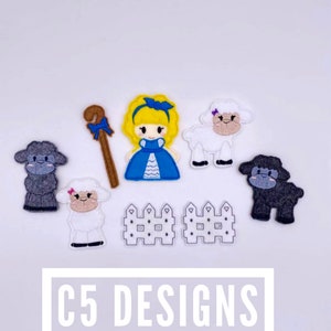 May include: Five felt finger puppets: a girl with blonde hair wearing a blue dress, a brown shepherd's crook, two white sheep, and one black sheep. Two white picket fences are also included. The text "C5 DESIGNS" is at the bottom of the image.