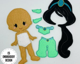 May include: A felt craft set featuring a brown-skinned doll with black hair, a white dress, and a green outfit. The set includes a headband, a top, pants, and two pairs of eyes.