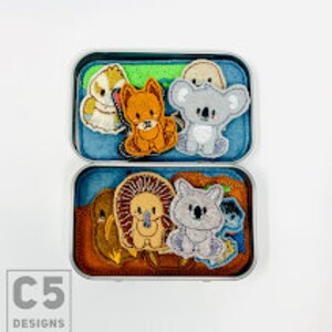 May include: A tin box filled with felt finger puppets of Australian animals, including a koala, a wombat, a kookaburra, and a echidna. The box has a green and brown background with a C5 Designs logo.