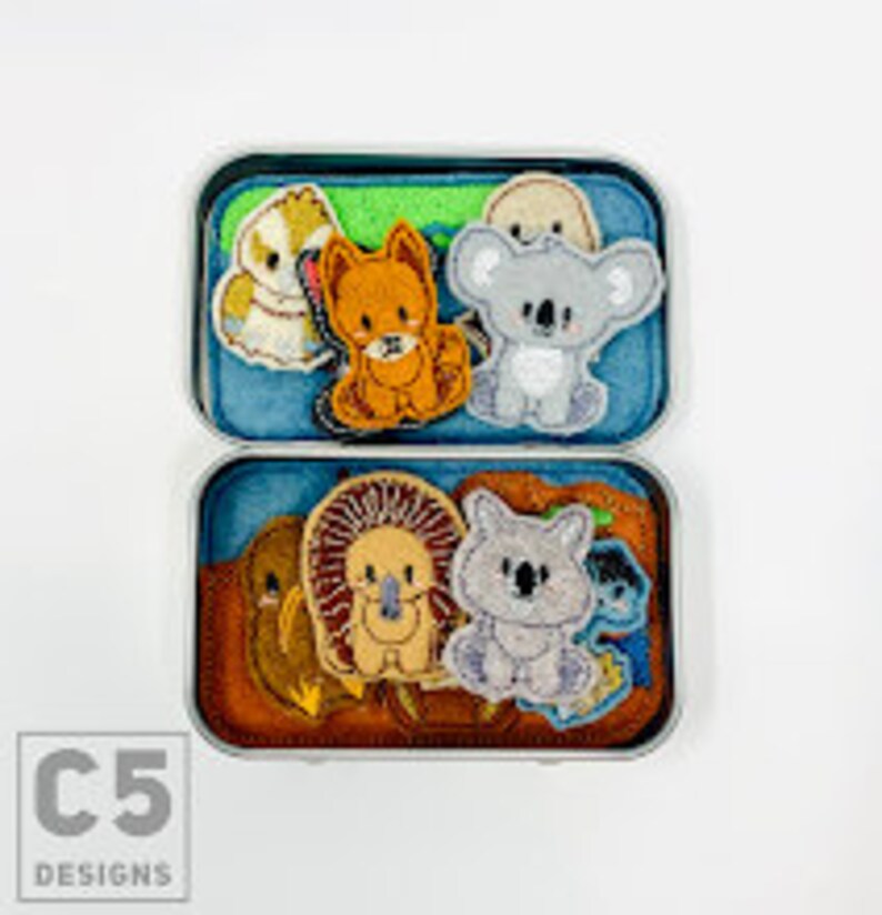 May include: A tin box filled with felt finger puppets of Australian animals, including a koala, a wombat, a kookaburra, and a echidna. The box has a green and brown background with a C5 Designs logo.