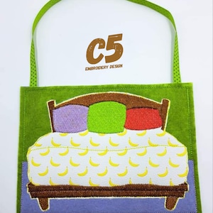 May include: A green felt appliqu&eacute; with a brown bed with three pillows, one purple, one green, and one red. The bed has a white sheet with a yellow banana pattern. The appliqu&eacute; has a green felt loop for hanging. The text "C5 EMBROIDERY DESIGN" is in brown text at the top.