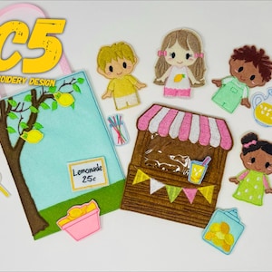 May include: A felt lemonade stand playset with a light blue bag, a brown tree, and a pink bowl of lemons. The set includes a lemonade stand, several felt figures, and a lollipop. The text "Lemonade 25c" is visible.