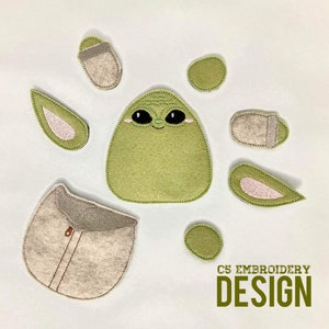 May include: Felt applique pieces for a baby Yoda embroidery project. The pieces include a green Yoda head, two pink ears, a brown pouch, and two green circles.