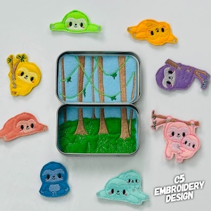 May include: A set of felt sloth finger puppets in various colours, including green, yellow, purple, pink, and blue. The puppets are arranged around a small metal tin with a felt scene of a jungle with trees and vines. The tin is open and the scene is visible. The text "C5 EMBROIDERY DESIGN" is visible in the bottom right corner of the image.