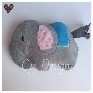 May include: A gray plush elephant toy with pink ears and a blue and yellow patterned saddle. The elephant has a small tail with a gray ribbon.