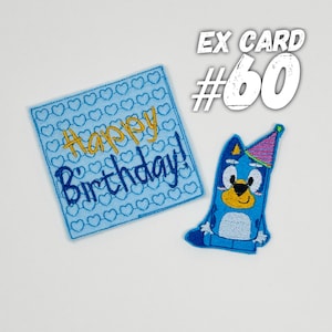 May include: Blue felt card with a white heart pattern and the text "Happy Birthday!" in yellow and blue embroidery. A blue felt character with a pink party hat is also included.