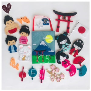 May include: A felt play set with Japanese cultural themes. It includes a red torii gate, a white cat, a red and white fan, a red lantern, a pink cherry blossom branch, a blue origami crane, a red and white Japanese flag, a mountain scene, and several finger puppets. The finger puppets include a sumo wrestler, a woman in a kimono, and a man in a blue shirt.