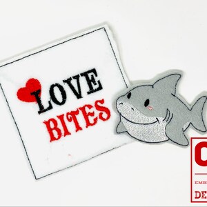 May include: Embroidered iron-on patch with a gray shark and a red heart with the text "Love Bites" in black and red lettering.