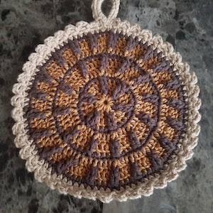 May include: A crocheted pot holder with a brown and gold circular design and a white crocheted border.