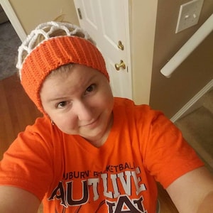 May include: A crochet headband featuring a wide orange ribbed band and a white net-like top section. The orange t-shirt displays the text AUBURN BASKETBALL with the letters AUTLIVE and a large letter A logo over a basketball graphic design.