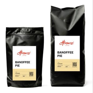 May include: Two black coffee bags with white labels. The labels read "Hormozi coffee" and "Banoffee Pie". The smaller bag is on the left, and the larger bag is on the right. The bags are sealed and appear to contain coffee beans.