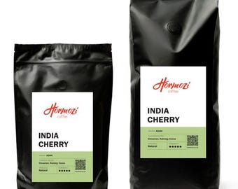 May include: Two black coffee bags with white labels. The labels read "Hormozi coffee" and "INDIA CHERRY". The smaller bag has a label with the text "ASIAN" and "Cinnamon, Nutmeg, Cocoa". The larger bag has the same information.