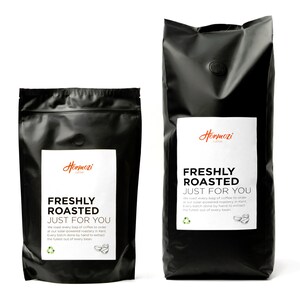 K&ouml;nnte beinhalten: Zwei schwarze Kaffeet&uuml;ten mit wei&szlig;en Etiketten. Auf den Etiketten steht "Hormozi Coffee" und "FRESHLY ROASTED JUST FOR YOU". Die T&uuml;ten haben eine matte Oberfl&auml;che und ein kleines, kreisf&ouml;rmiges Ventil. Der Text erw&auml;hnt auch das R&ouml;sten mit Solarenergie.
