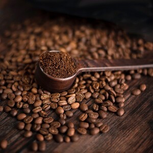 K&ouml;nnte beinhalten: Ein h&ouml;lzerner L&ouml;ffel, gef&uuml;llt mit gemahlenem Kaffee, liegt auf einem Bett aus ger&ouml;steten Kaffeebohnen. Der L&ouml;ffel und die Bohnen befinden sich auf einer dunklen Holzoberfl&auml;che. Das Bild hebt die satten Braunt&ouml;ne von Kaffee und Holz hervor.