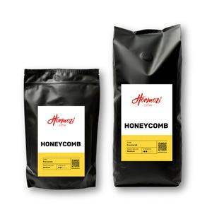 May include: Two black coffee bags with white labels. The labels display the brand name "Hormozi coffee" and the word "HONEYCOMB" in bold letters. The bottom of the label has a yellow stripe with additional text and a QR code.