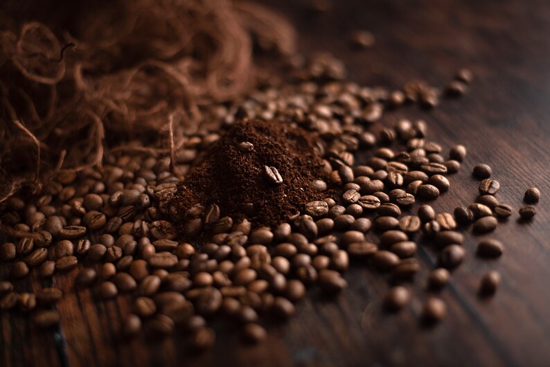 K&ouml;nnte beinhalten: Nahaufnahme von Kaffeebohnen und gemahlenem Kaffee auf einer dunklen Holzoberfl&auml;che. Die ger&ouml;steten Kaffeebohnen umgeben einen kleinen Haufen gemahlenen Kaffees, mit ein paar Bohnen obenauf. Das Bild hat eine warme, einladende Ausstrahlung.