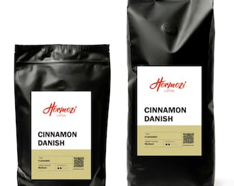 May include: Two black coffee bags with white labels. The labels read "Hormozi coffee" and "Cinnamon Danish". The bags are sealed and have a small, round, dark-colored closure. The coffee is flavored and medium roast.