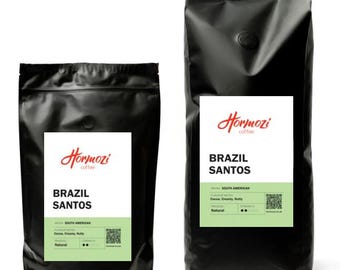 May include: Two black coffee bags with white labels. The labels read "Hormozi coffee" and "BRAZIL SANTOS". The smaller bag has a label with "SOUTH AMERICAN" and "Natural" printed on it. The larger bag has the same text, plus "Cocoa, Creamy, Nutty".