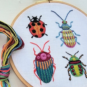 May include: Embroidered hoop art featuring four colorful insects: a ladybug, a green and orange beetle, a blue and yellow beetle, and a green and red beetle.