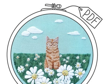 May include: A cross-stitch embroidery hoop with a cute orange cat sitting in a field of white daisies. The cat is smiling and has green eyes. The background is a light blue sky with white clouds.