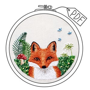 May include: Embroidered hoop art featuring a fox with orange fur, white chest, and black eyes. The fox is surrounded by green foliage, a red mushroom, and blue butterflies. The hoop is outlined in black and the word "PDF" is written in black on a white tag.