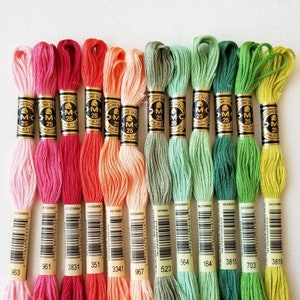 May include: Ten spools of DMC embroidery floss in various shades of pink, orange, green, and yellow. Each spool has a black and gold label with the DMC logo and the number of the color.