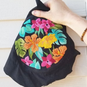 May include: Black fabric with embroidered tropical flowers in shades of pink, yellow, green, and blue. The flowers are detailed and realistic.