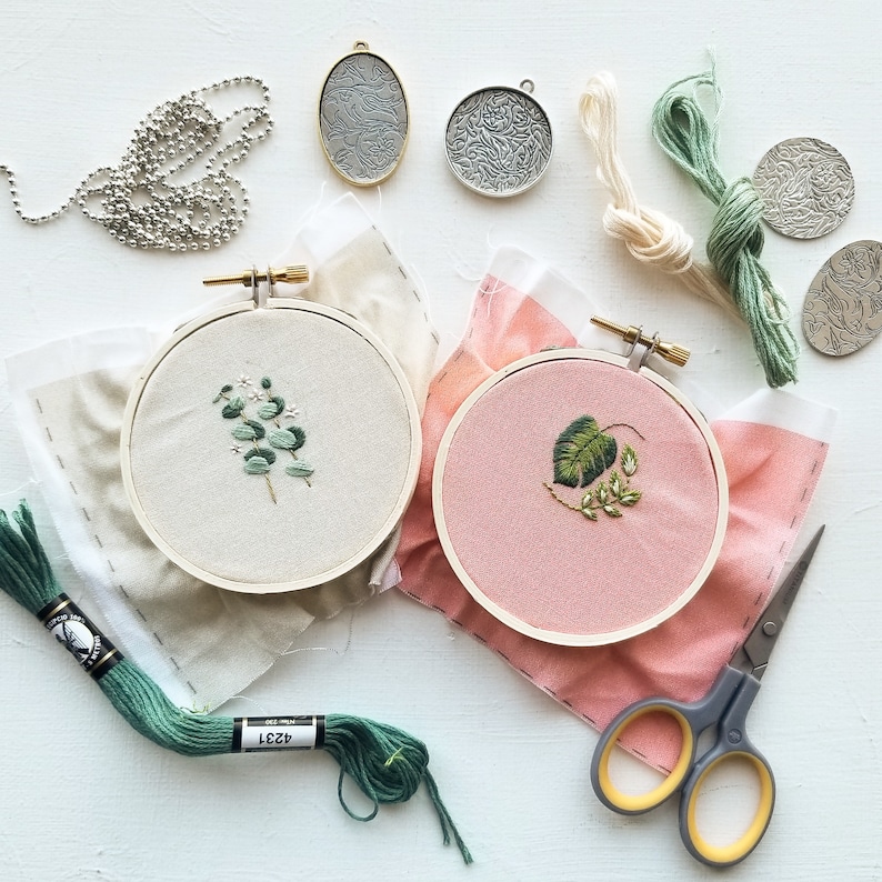 Puede incluir: Dos aros de bordado con diferentes dise&ntilde;os florales. El aro de la izquierda tiene un dise&ntilde;o floral verde sobre fondo blanco. El aro de la derecha tiene un dise&ntilde;o floral verde sobre fondo rosa. Ambos aros est&aacute;n sobre tela.