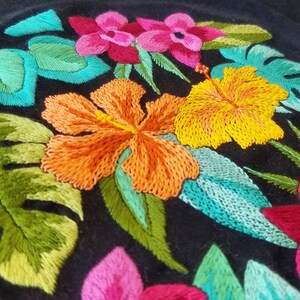 May include: Embroidered floral design on black fabric featuring pink, yellow, and orange flowers with green leaves.