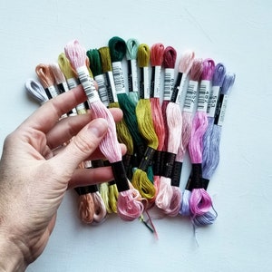 Pode incluir: Uma cole&ccedil;&atilde;o de carret&eacute;is de fio de bordado em v&aacute;rias cores, incluindo rosa, verde, azul e marrom. Os carret&eacute;is s&atilde;o etiquetados com n&uacute;meros e a palavra "Cotone".