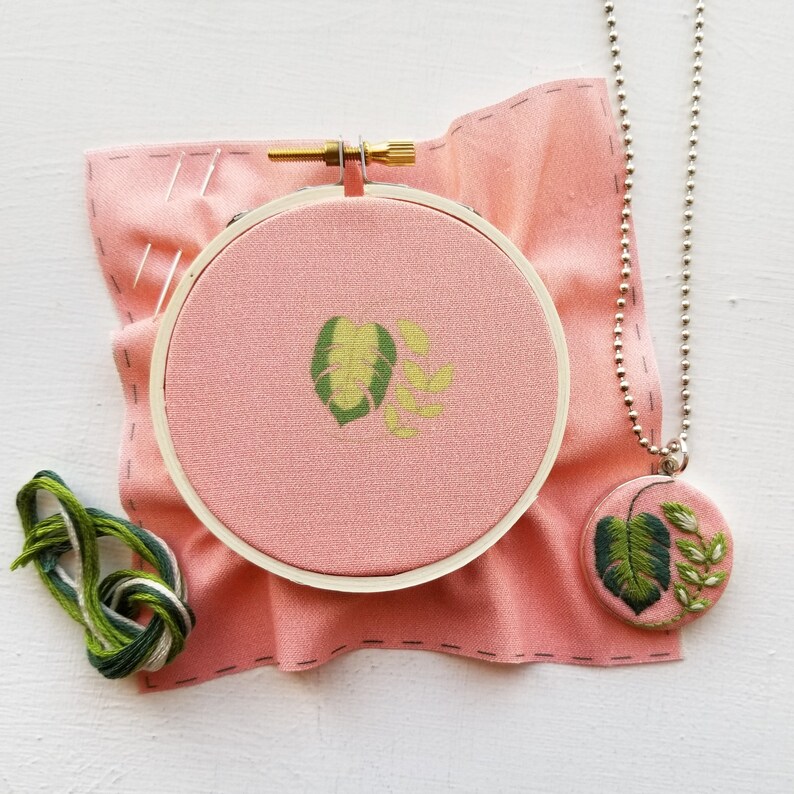 Puede incluir: Un aro de tela rosa con un dise&ntilde;o de hoja bordada en verde y amarillo. Tambi&eacute;n se incluye un collar de cadena plateada con un colgante a juego.