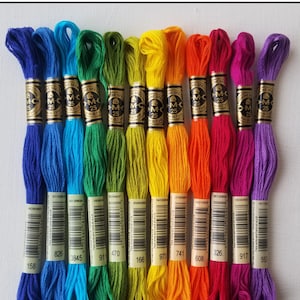 May include: A vibrant display of DMC embroidery threads in a spectrum of colours, from deep blues to vibrant purples. The image is titled "Iris Palette August 2022 DMC Bundle of the Month". Each skein is labelled with a number.