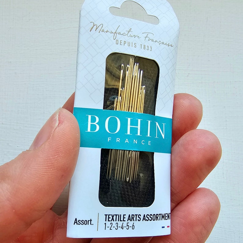 May include: A package of Bohin Textile Arts Assortment needles, size 1-2-3-4-5-6, made in France. The package is white with blue and red accents and features the Bohin logo.