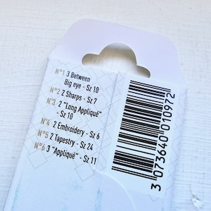 May include: Close-up of a white product label with black text listing different needle sizes and types. The label also includes a black and white barcode with the number 3073640 010972.