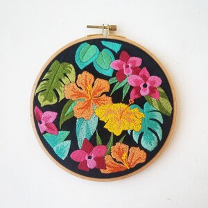 May include: Embroidered hoop art featuring a tropical floral design with pink, orange, yellow, and green flowers on a black background.