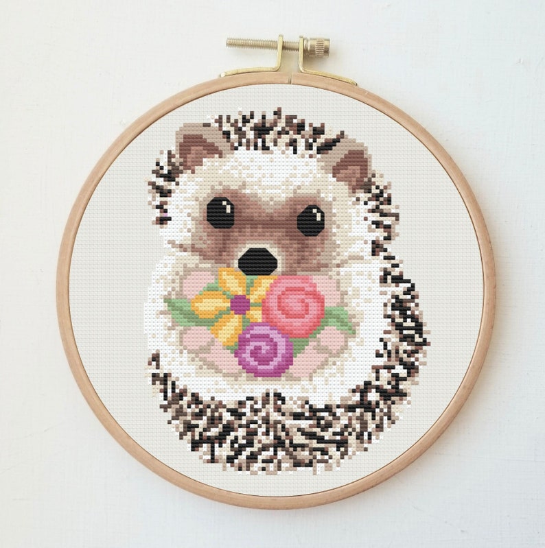 May include: A cross-stitch pattern of a cute hedgehog holding a bouquet of colourful flowers. The hedgehog is brown and white with black eyes and a black nose. The flowers are pink, yellow and purple.