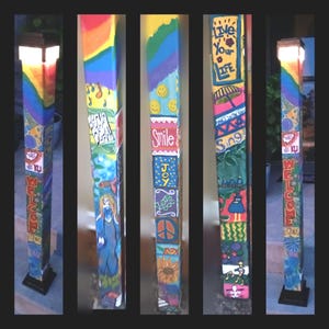 May include: A collection of brightly painted wooden posts with built-in lights. Each post displays unique designs, including rainbows, musical notes, smiley faces, and the words "Welcome," "Smile," and "Joy." The posts are decorated with various artistic elements.