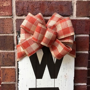 May include: A white wooden sign with the word "WELCOME" painted in black. A large red and white gingham bow is tied to the top of the sign.