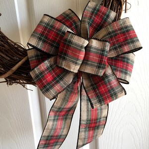 May include: A decorative wreath with a large plaid bow. The bow features a red, green, and tan plaid pattern with black trim. The wreath base is made of interwoven brown twigs.