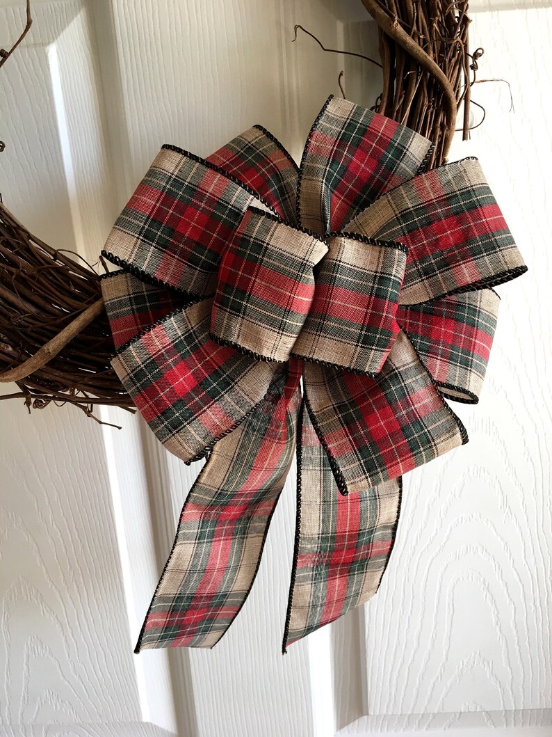 May include: A decorative wreath with a large plaid bow. The bow features a red, green, and tan plaid pattern with black trim. The wreath base is made of interwoven brown twigs.