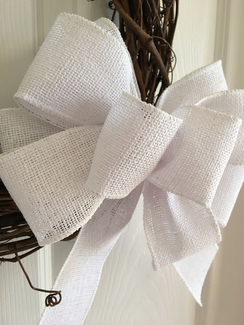 May include: A white burlap bow with a woven texture is tied around a brown twig wreath.