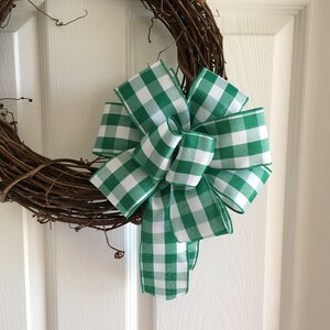 May include: A green and white gingham bow tied on a grapevine wreath. The bow is made of a thick, woven ribbon.