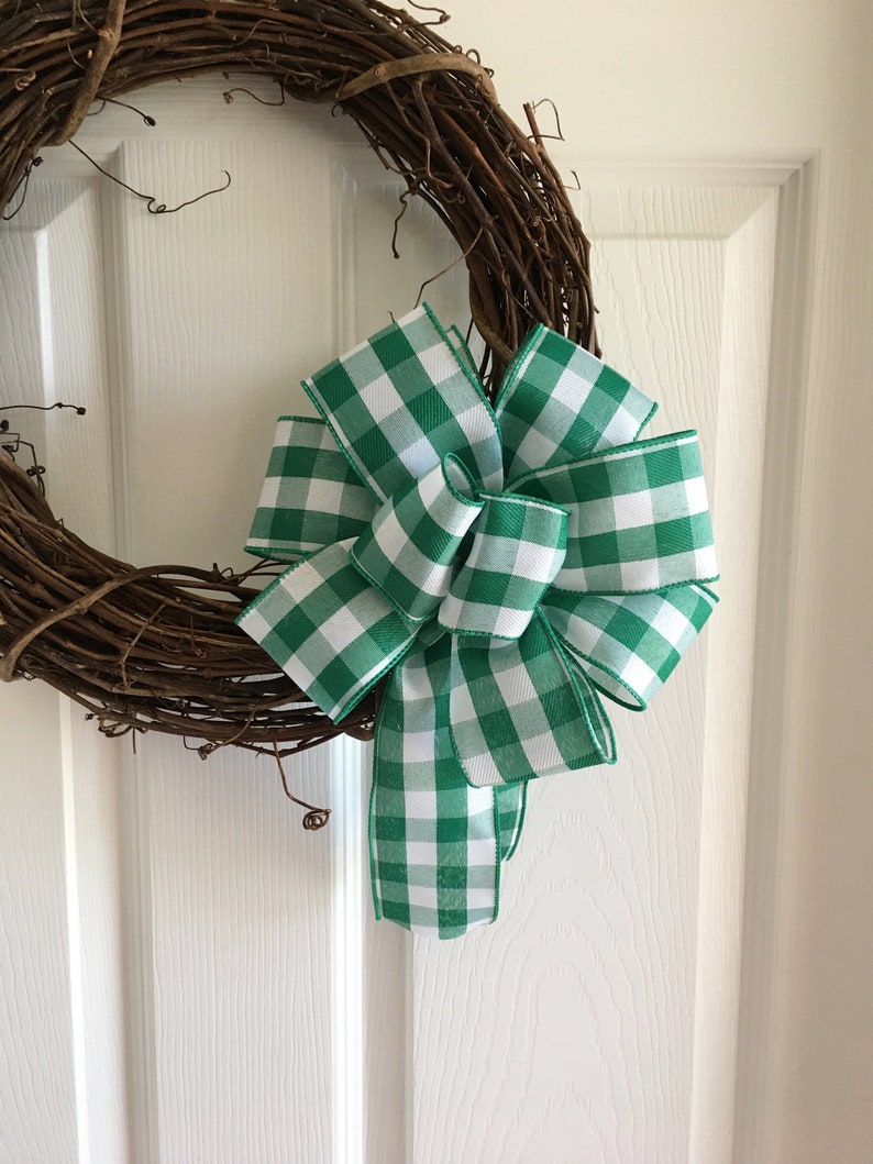 May include: A green and white gingham bow tied on a grapevine wreath. The bow is made of a thick, woven ribbon.