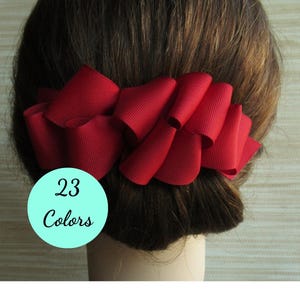 May include: A deep red hair accessory made of ribbed fabric, featuring multiple folded loops arranged in a wide, horizontal design. A circular light blue graphic overlay on the lower left side displays the text 23 Colors in black script.