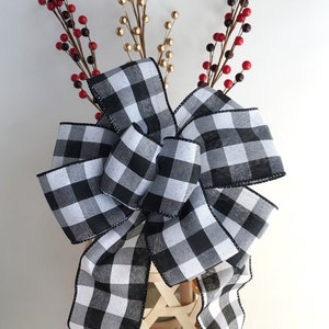 May include: A large black and white buffalo plaid bow with a black trim. The bow is tied around a wicker basket with red and gold berry sprigs.
