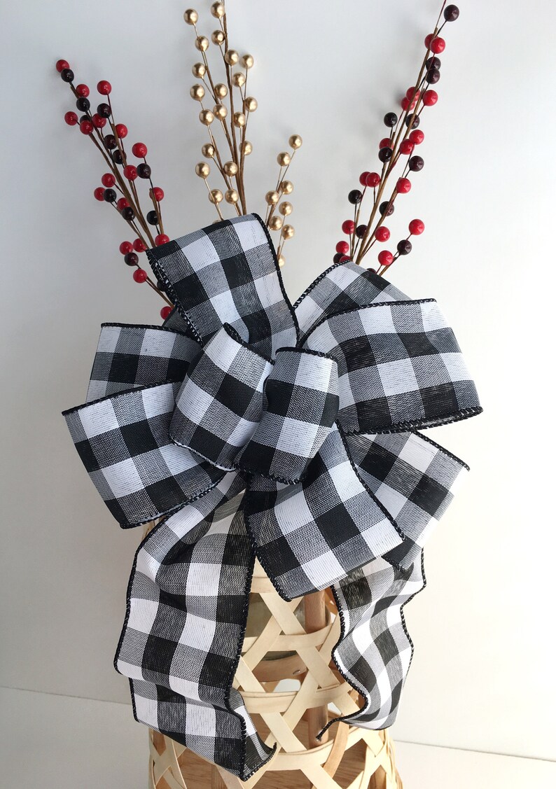 May include: A large black and white buffalo plaid bow with a black trim. The bow is tied around a wicker basket with red and gold berry sprigs.