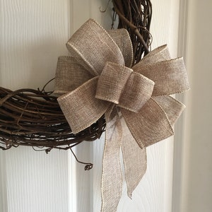 May include: A brown grapevine wreath with a large burlap bow. The bow is tied with a double knot and has long tails.
