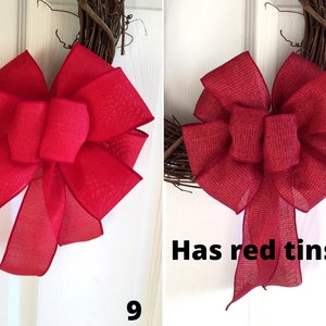 May include: Two red burlap bows on a grapevine wreath. The bow on the right has red tinsel.